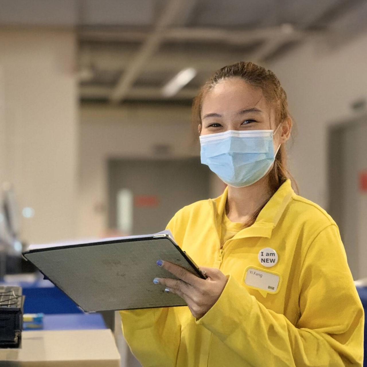 A IKEA service staff wearing a mask in IKEA's iconic yellow jacket holding a tablet. 