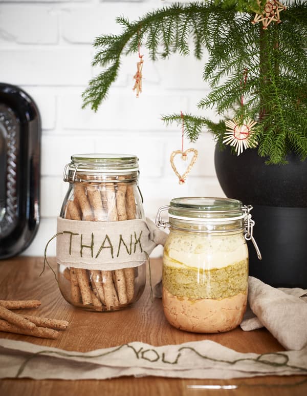 A jar of crisp breadsticks and a jar of layers of different flavours of hummus decorated with fabric thank-yous.