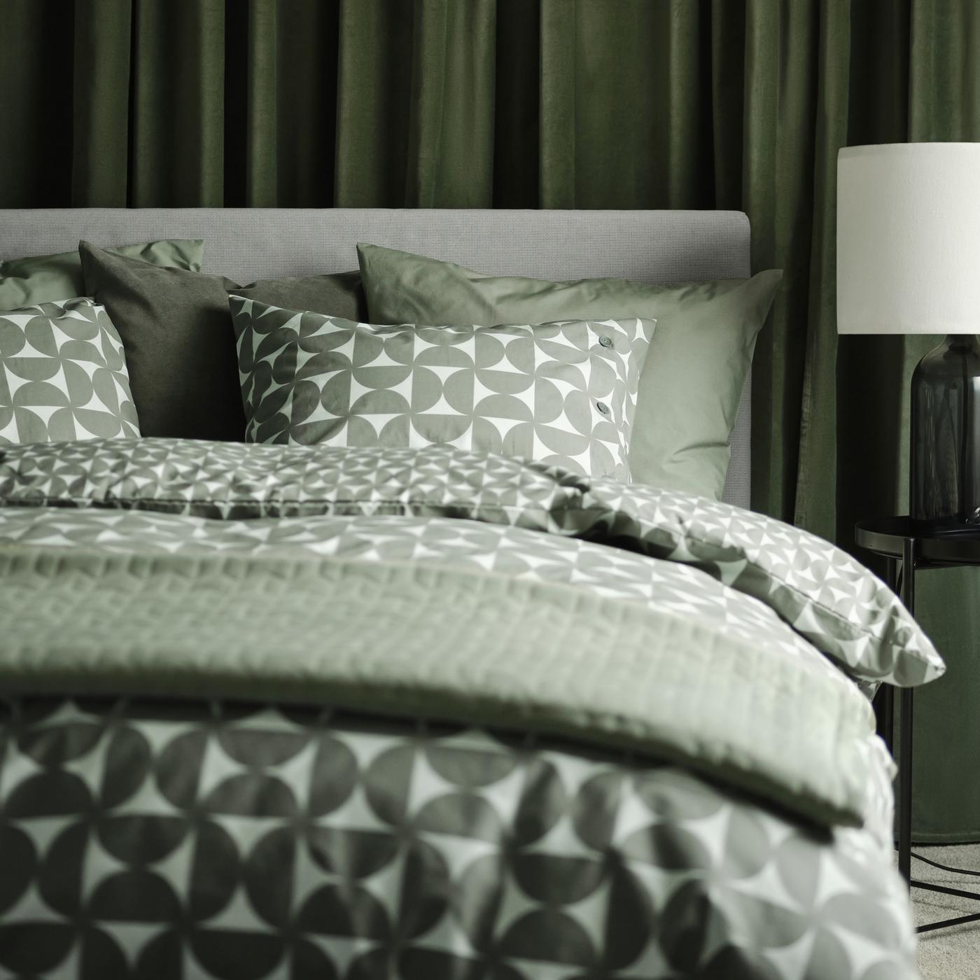 A Kabusa light grey GLADSTAD upholstered bed with four storage boxes dressed in grey/green ÄNGSNEJLIKA bed linen.