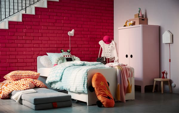 A kid's bedroom set up for a sleepover including a bed with storage, a futon, a pink wardrobe, and a dressform