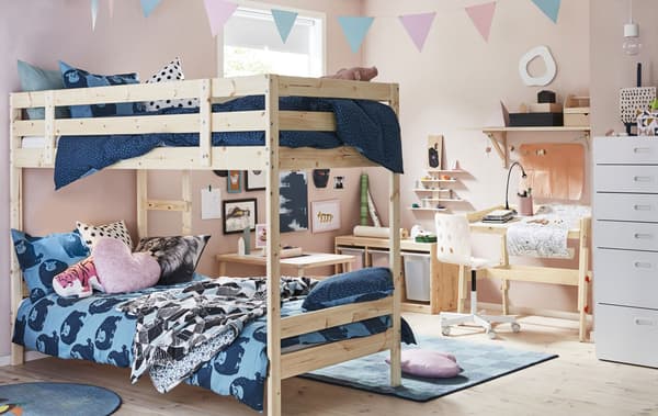 A kid’s bedroom with pink walls, bunk bed with blue bedding, and light wood desk and storage.
