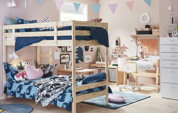 A kid’s bedroom with pink walls, bunk bed with blue bedding, and light wood desk and storage.