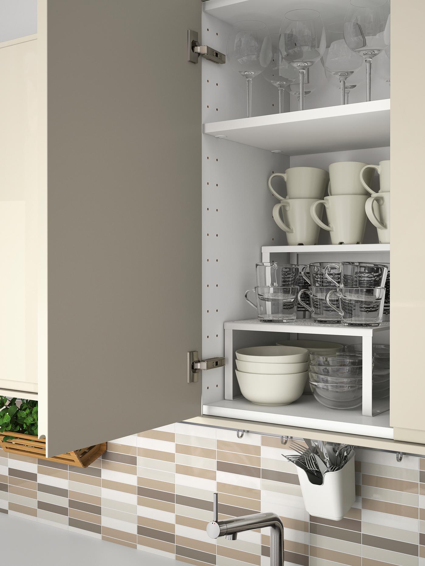 A kitchen cabinet with an open high-gloss light-beige door, showing tableware stored inside on shelves.