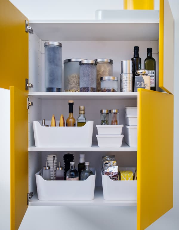 A kitchen cabinet with yellow doors is organised with white plastic bins.