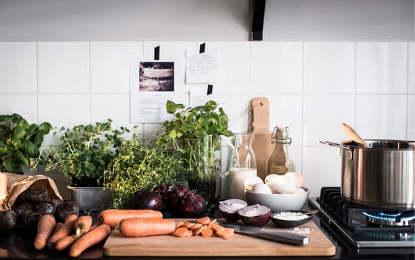 A kitchen counter top and wooden cutting board piled high with fresh vegetables and herbs.