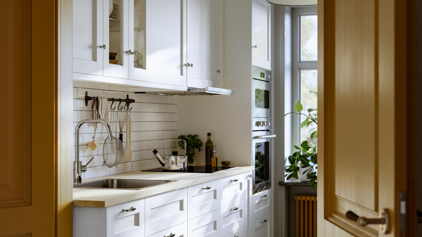 A kitchen has drawers and wall cabinets with white ENKÖPING fronts and a nickel-plated HULTARP rail with hooks on the wall.