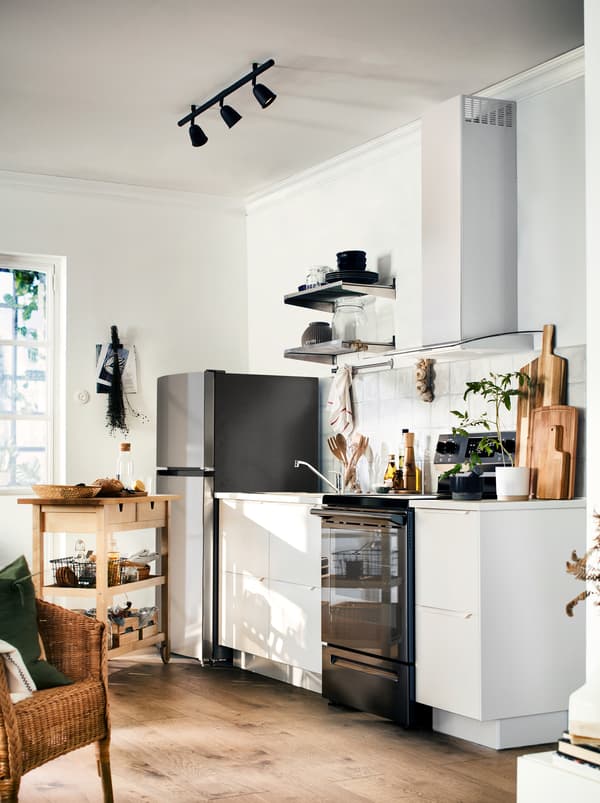 A kitchen in white and black with warm wood tones from the floor, the worktop, and a FÖRHÖJA wooden kitchen trolley.