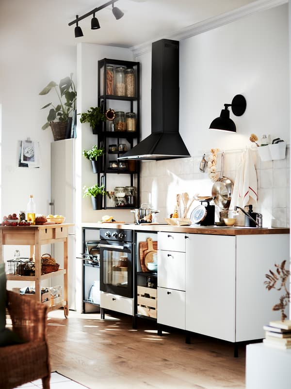 A kitchen in white and black with warm wood tones from the floor, the worktop, and a FÖRHÖJA wooden kitchen trolley.