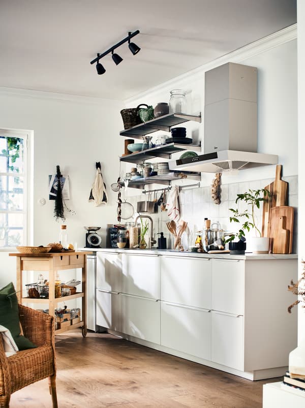 A kitchen in white and grey with warm wood tones from the floor, accessories, and a FÖRHÖJA wooden kitchen trolley.