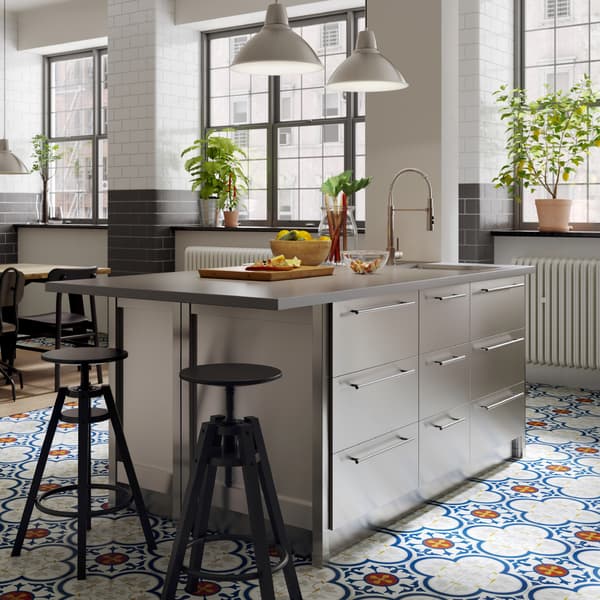 A kitchen island with worktop in concrete effect/quartz and drawers in stainless steel. Two black bar stools stand beside.