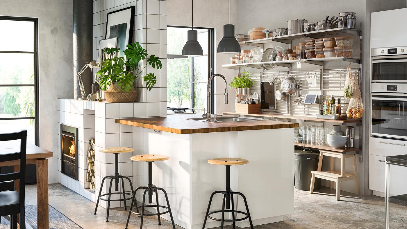 A kitchen with a high-gloss white/wood island, a stainless steel wall-mounted grid with shelves, and stools in pine/black.