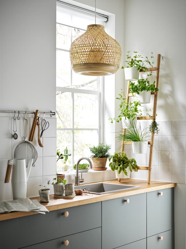 A kitchen with a ladder-like SATSUMAS bamboo plant stand with five plant pots standing on the worktop in front of a window.