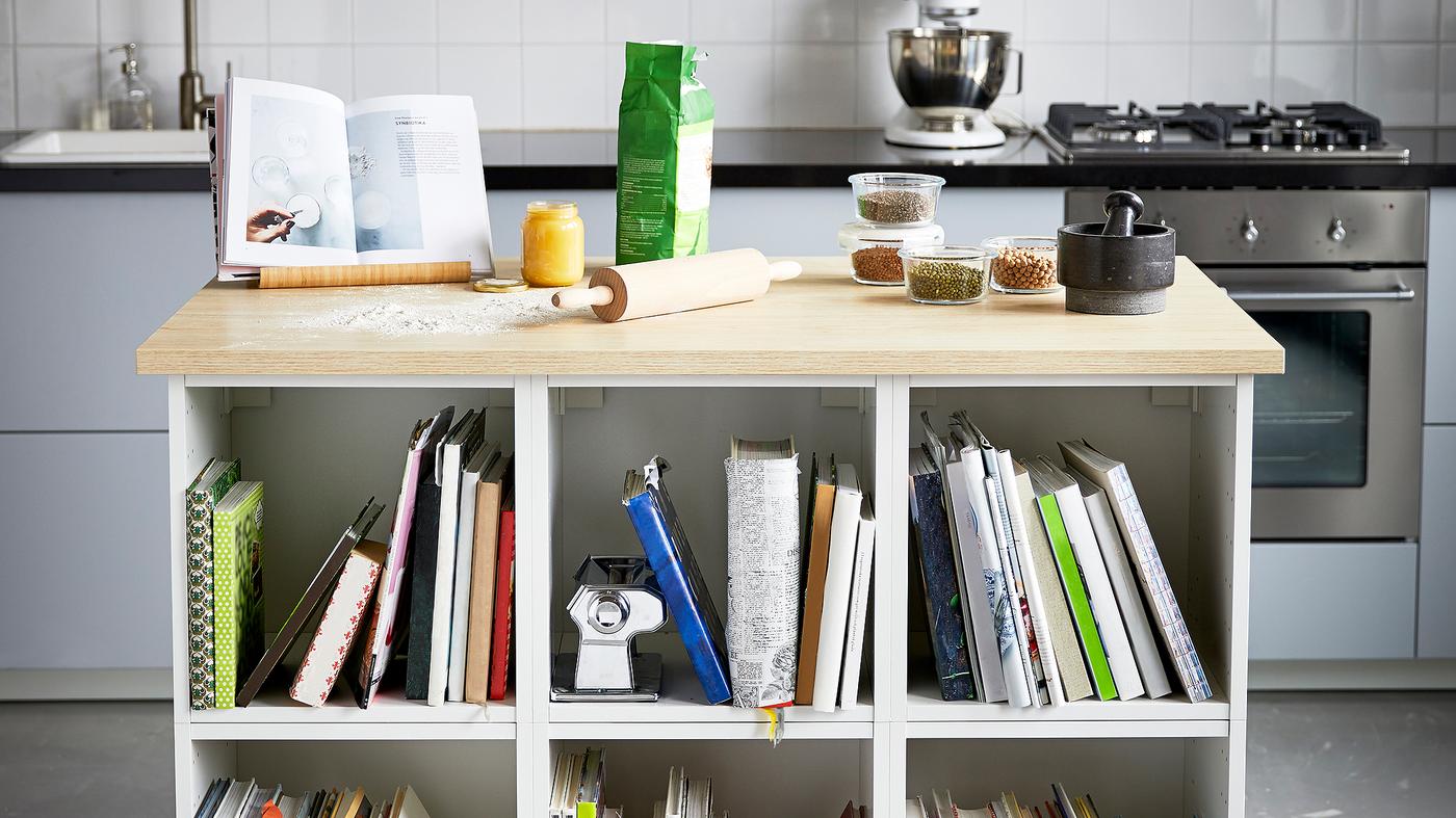 A kitchen with a white island with a wood worktop with baking tools, glass containers and a black pestle and mortar.