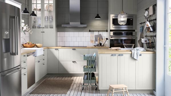 A kitchen with beige door fronts, wood countertops and stainless appliances with white tile against the wall.