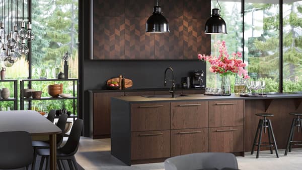 A kitchen with brown fronts and large windows, with two black pendant lamps and a vase of flowers on the kitchen island.