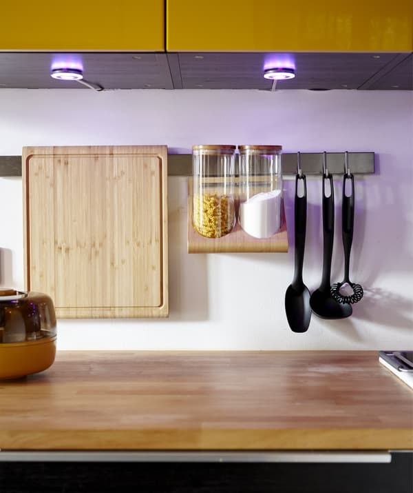 A kitchen with cupboard spotlights and a hanging utensils rack.