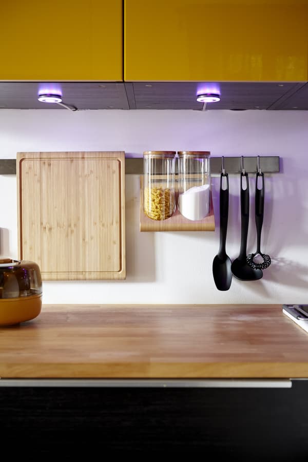A kitchen with cupboard spotlights and a hanging utensils rack.