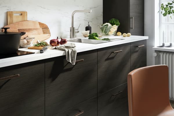 A kitchen with fronts in dark brown ash effect and a wall panel in white marble effect, a wooden table and leather chairs.