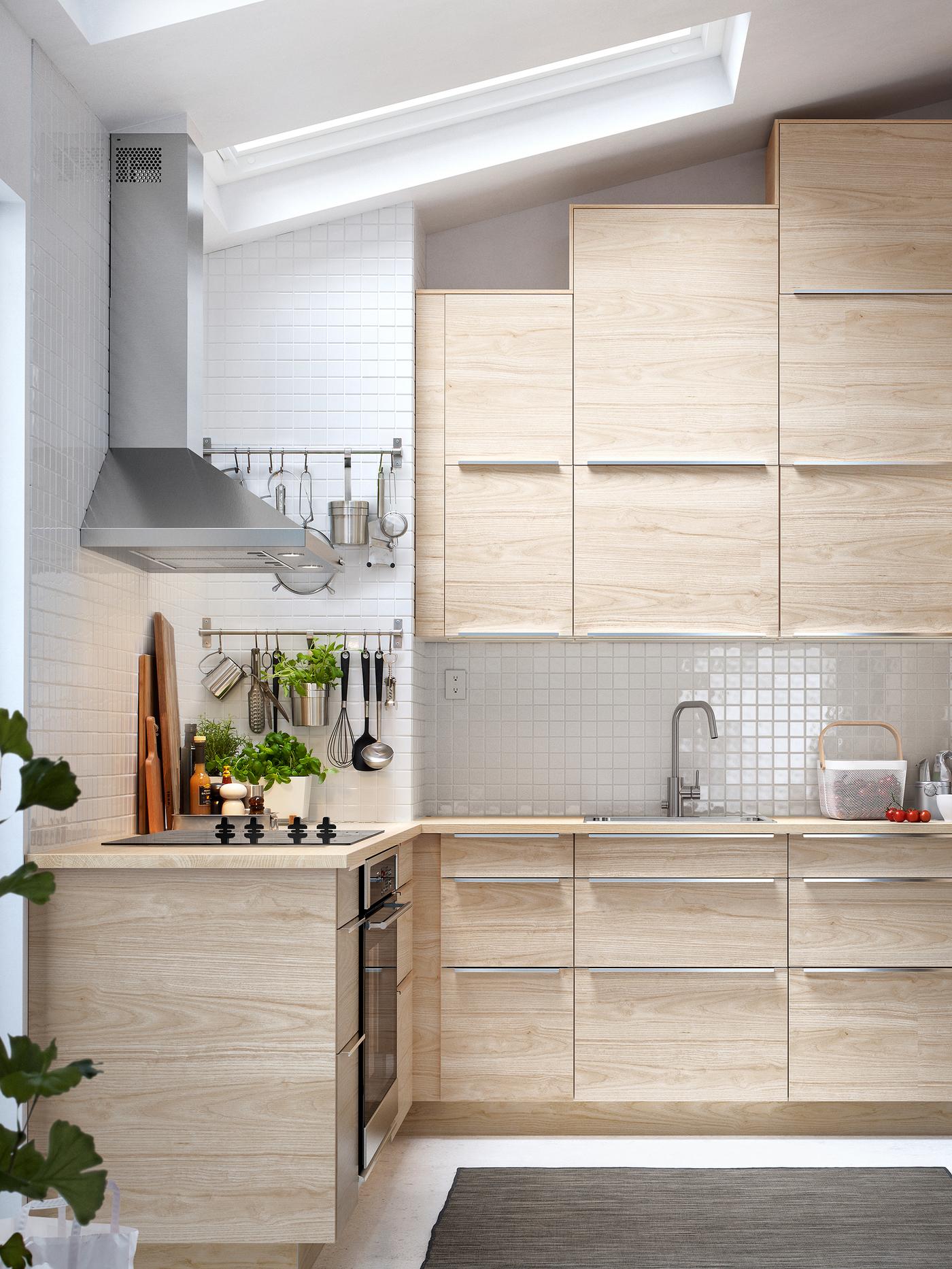 A kitchen with IKEA SEKTION cabinets with ASKERSUND light ash wood-effect fronts and an extractor hood in stainless steel.