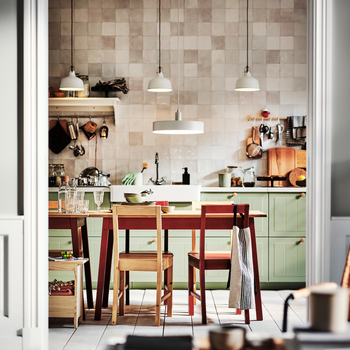 A kitchen with light green STENSUND drawer fronts and two PINNTORP tables surrounded by PINNTORP chairs.