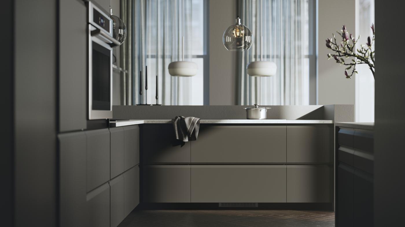 A kitchen with UPPLÖV anthracite kitchen fronts, BLÅSVERK pendant lamps in beige and an TÄNGBY wall oven in stainless steel.