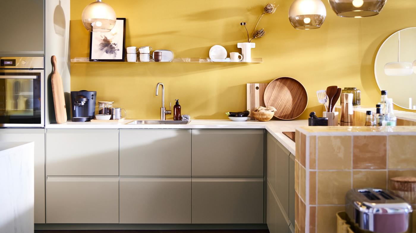 A kitchen with UPPLÖV fronts in dark beige and JAKOBSBYN pendant lampshades in frosted glass and grey and other kitchen items.