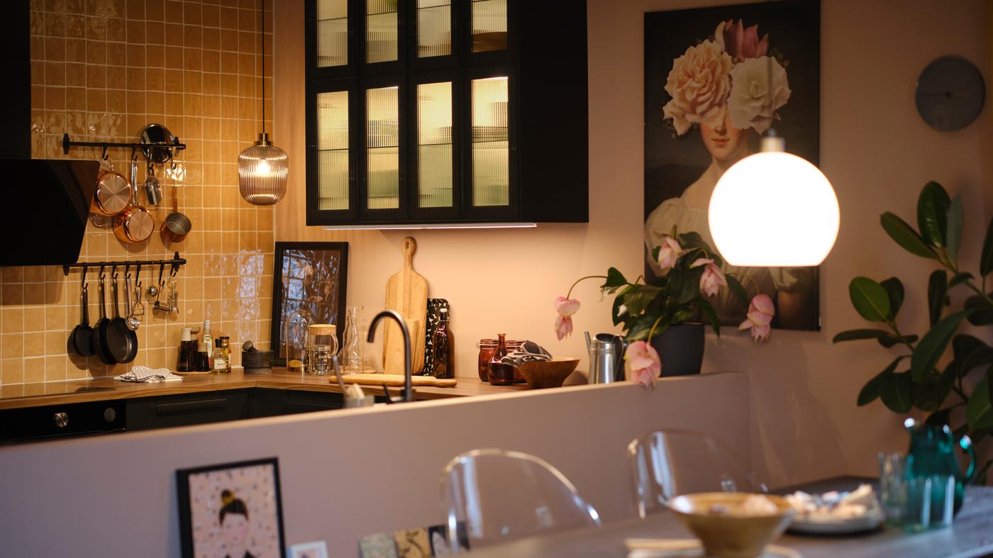 A kitchen with wall cabinets with glass doors and lighting inside, plus pendant lamps over the worktop and extendable table.