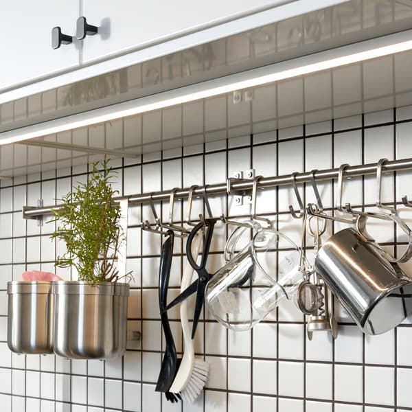 A kitchen with white cabinet doors, and under them is a white tile wall with a mounted rail and hooks in stainless steel.