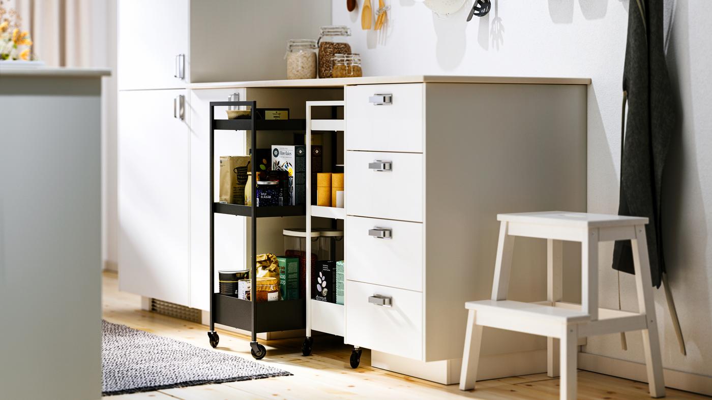A kitchen with white METOD base cabinets and MAXIMERA interiors, a KASKER worktop and two NISSAFORS trolleys.