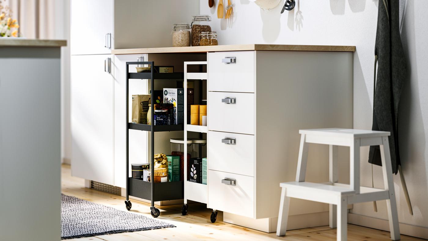 A kitchen with white METOD base cabinets and MAXIMERA interiors, an EKBACKEN worktop and two NISSAFORS trolleys.