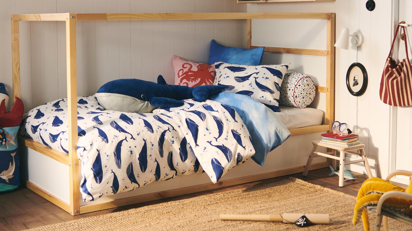 A KURA bed is dressed in a BLÅVINGAD blue whale duvet set; a BLÅVINGAD blue whale soft toy sits on top.