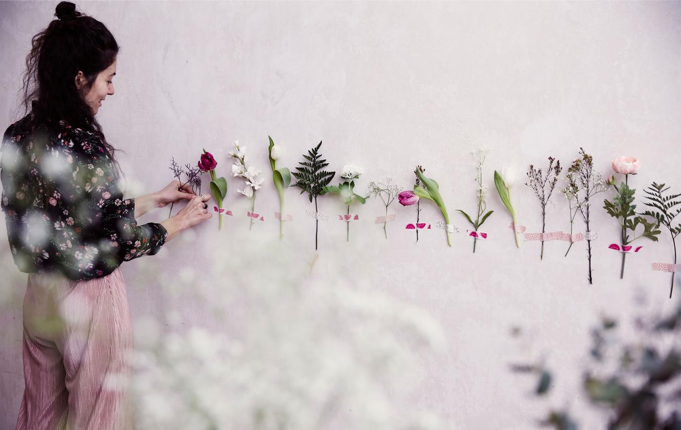 À l'aide de ruban adhésif, Julia colle des fleurs sur un mur blanc.