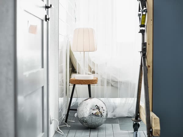 A lamp on a cork stool next to a bed dressed in white textiles and a loose disco ball.