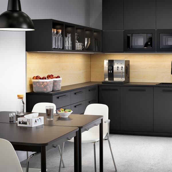 A large anthracite kitchen with drawers and cabinets, coffee machine, bowls with fruits and two tables with white chairs.