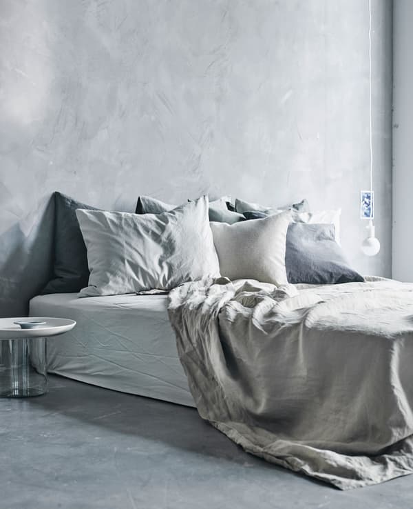 A large bed, low to the floor covered in light grey textiles.