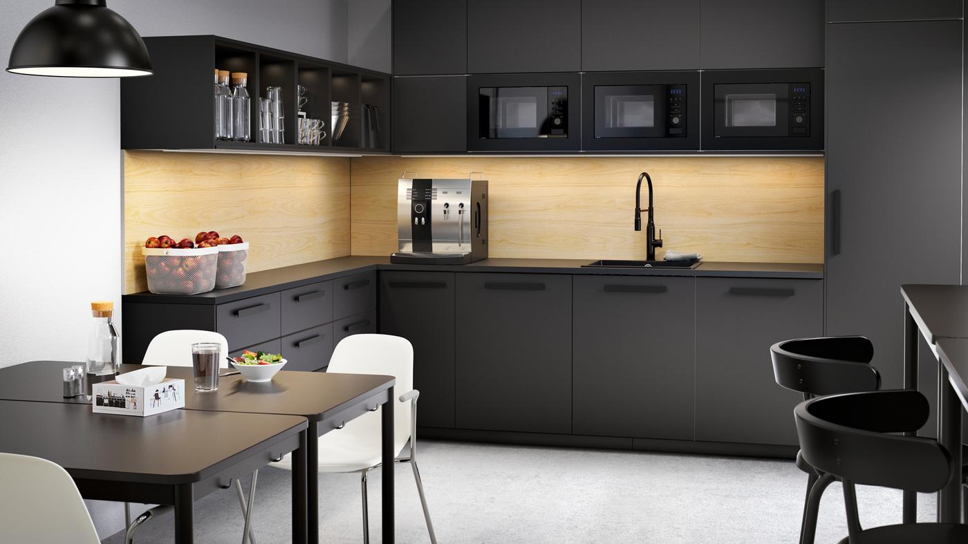 A large black kitchen with drawers and cabinets, coffee machine, bowls with fruits and two tables with white chairs.