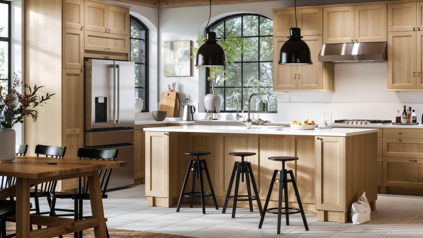 A large bright kitchen with VEDHAMN oak fronts and a kitchen island with two pendant lamps above it and bar stools in front.
