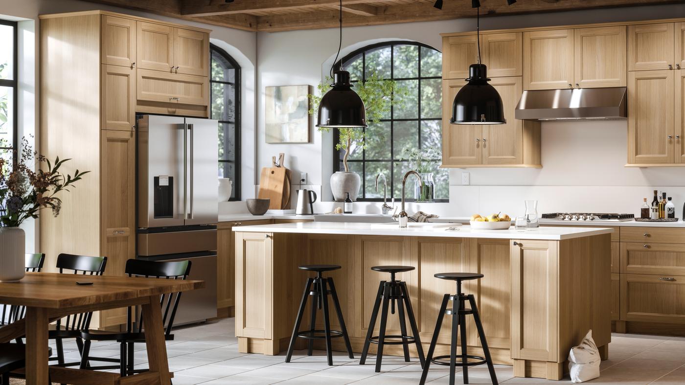 A large bright kitchen with VEDHAMN oak fronts and a kitchen island with two pendant lamps above it and bar stools in front.