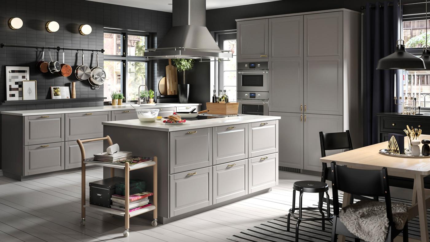 A large grey kitchen with a kitchen island in the centre and a beech/white dining table with black chairs and stools.