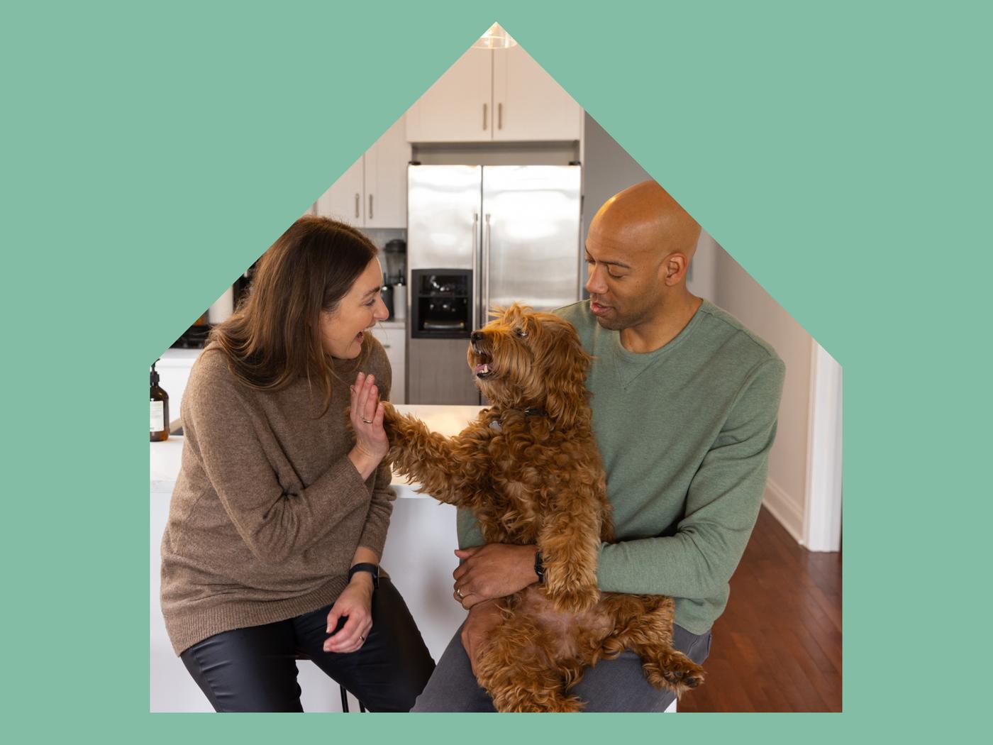 A large house shape with image of a young couple sitting in their kitchen laughing and playing with their small dog.