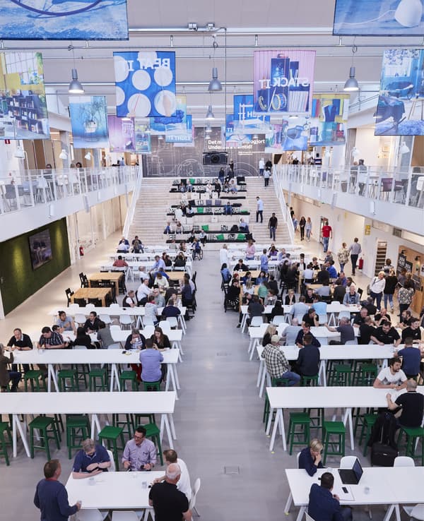 A large industrial space with people working alone and in groups, on benches, steps and tables.