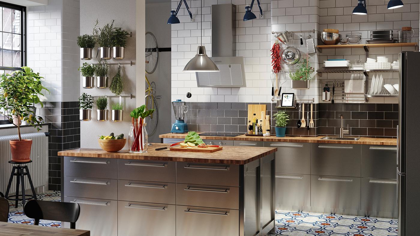 A large kitchen with fronts in stainless steel, worktops in oak/veneer, blue work lamps and herbs in containers.