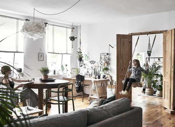 A large living area with desk, sofa, table and Hania on a swing in the doorway.