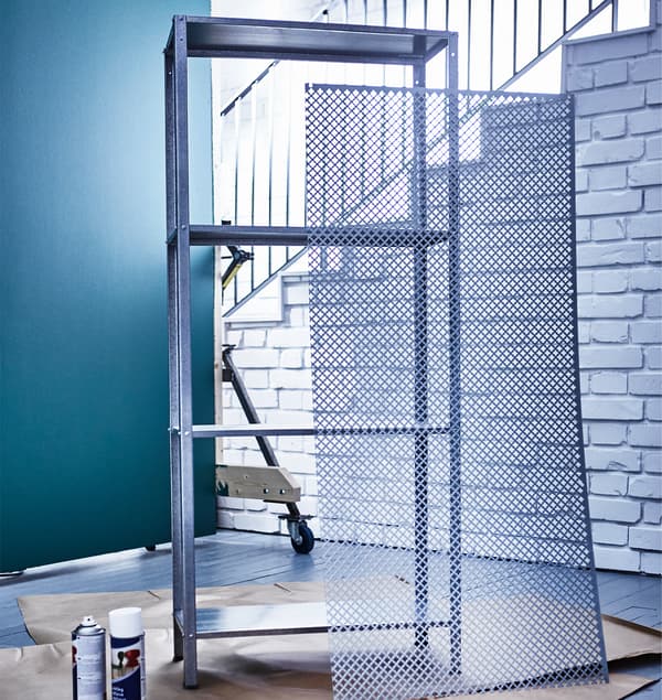 A large mesh metal sheet leans against an unpainted IKEA HYLLIS shelving unit.