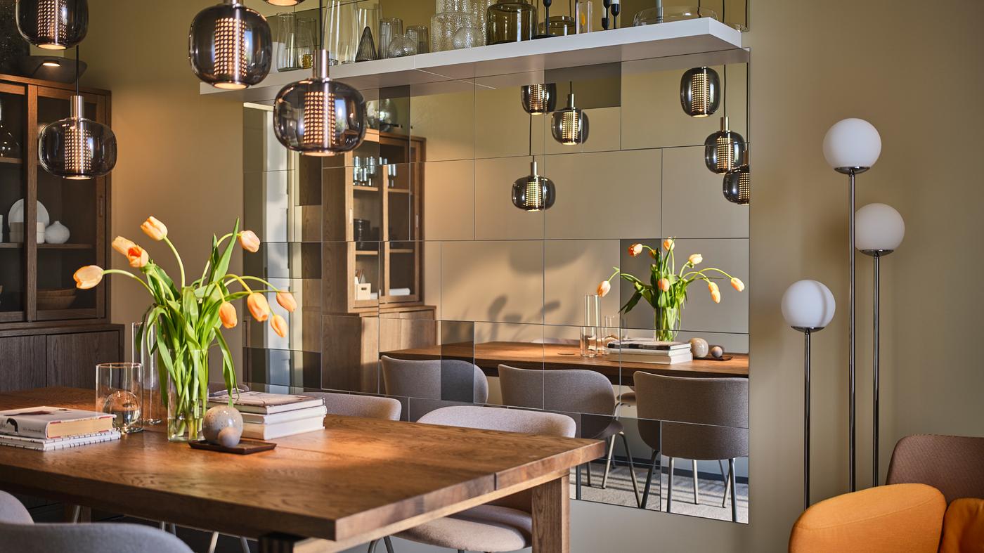 A large MÖRBYLÅNGA table sits in the center of a narrow yet sophisticated dining room with plenty of mirrors on one wall.