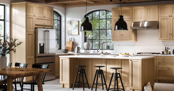 A large oak kitchen with black stools and black pendant lamps hanging over an island.
