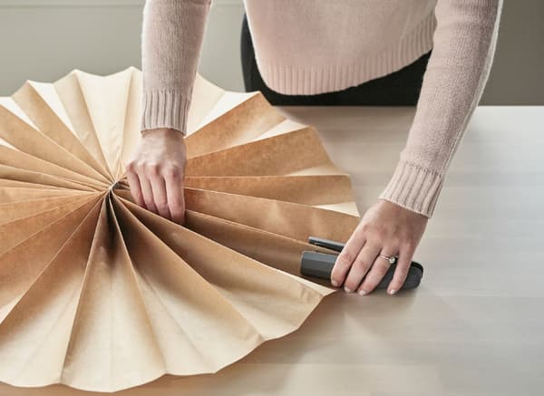 A large rosette being created with accordion folds and a stapler.