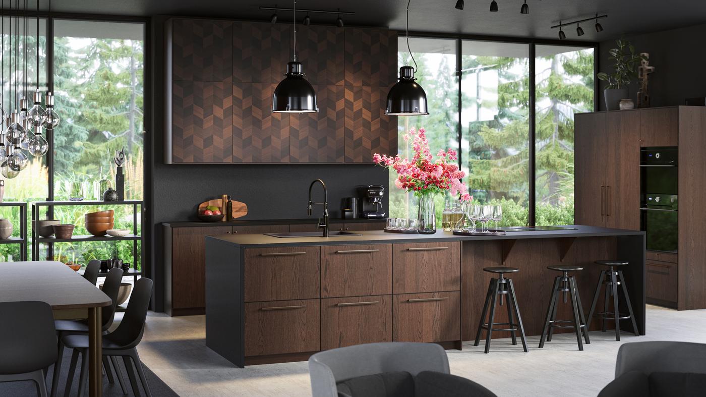 A large stylish kitchen island with wooden fronts. Black bar stools, black pendant lamps, a fridge with wooden doors.