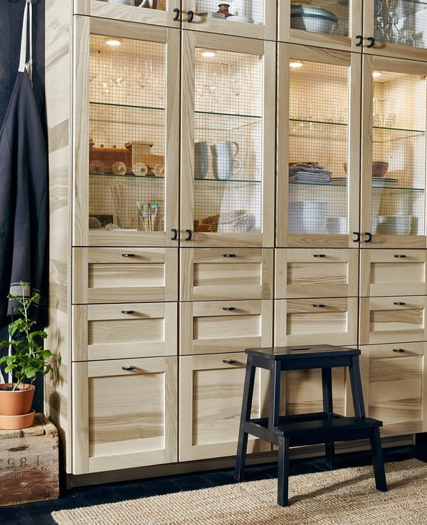 A large wall of kitchen storage with ash veneer drawers and glass-door cabinets.