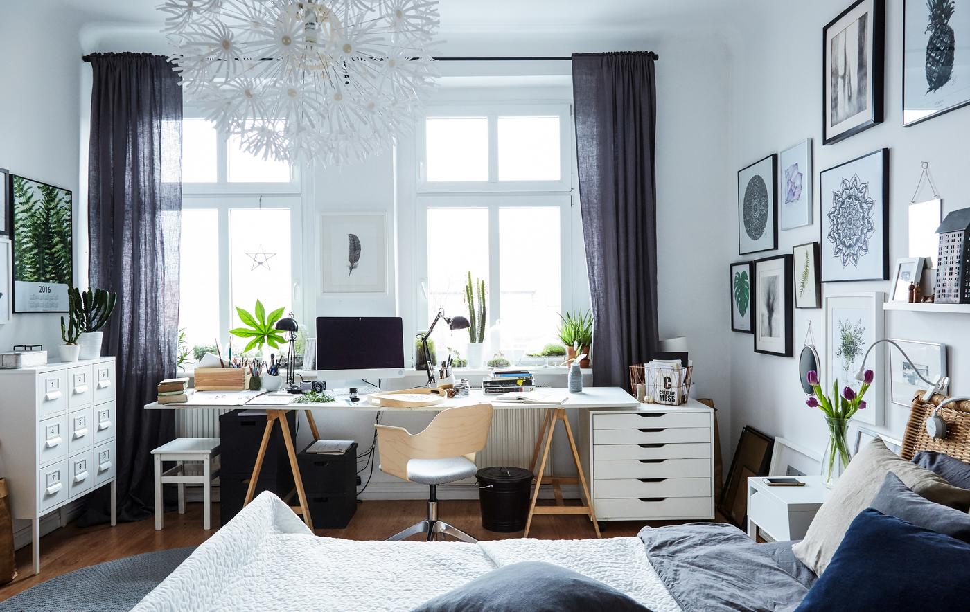 A large white bedroom with a home office space set in front of large windows.